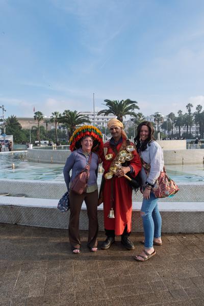 Street performer with brass instruments posing with two tourists by a fountain Casablanca, Morocco