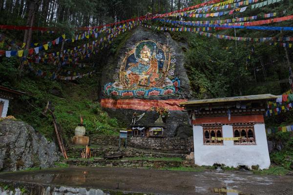 Rock mural of Guru Rinpoche with prayer flags in a forest shrine near Thimphu, Bhutan Boegarna_Dodennang, Bhutan