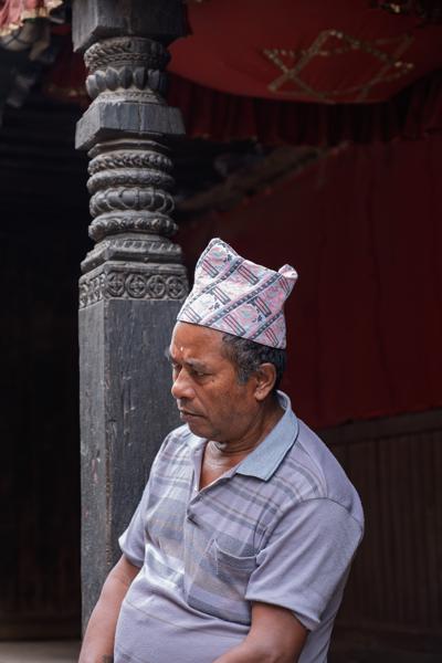 Nepalese man in a patterned topi beside an intricately carved wooden pillar Bhaktapur, Nepal
