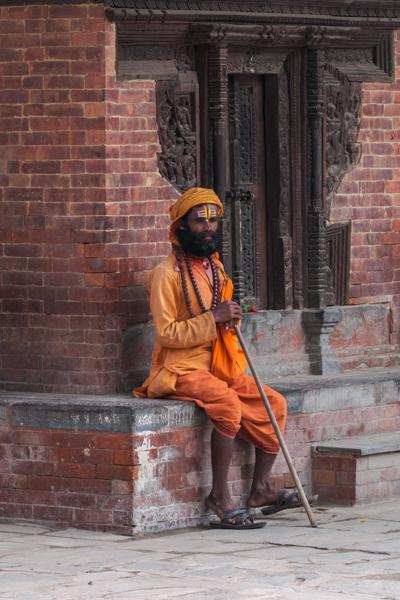 Hindu sadhu resting beside a carved temple doorway Kathmandu Metropolitan, Nepal