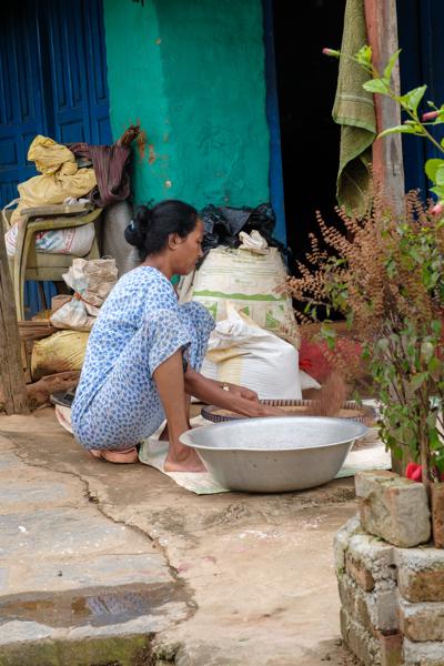 Woman Sorting Grains Outside a Turquoise-Walled Home Aanbu Khaireni, Nepal