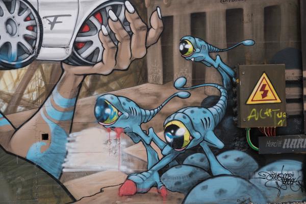 Blue alien graffiti mural with a car wheel and electrical box Bezirk Lebern, Switzerland